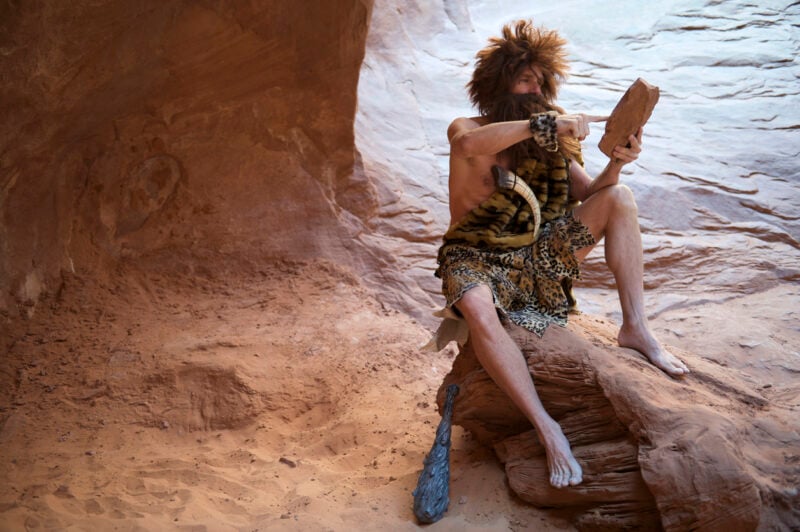 Caveman Sitting Outdoors Using Stone Tablet with Touchscreen
